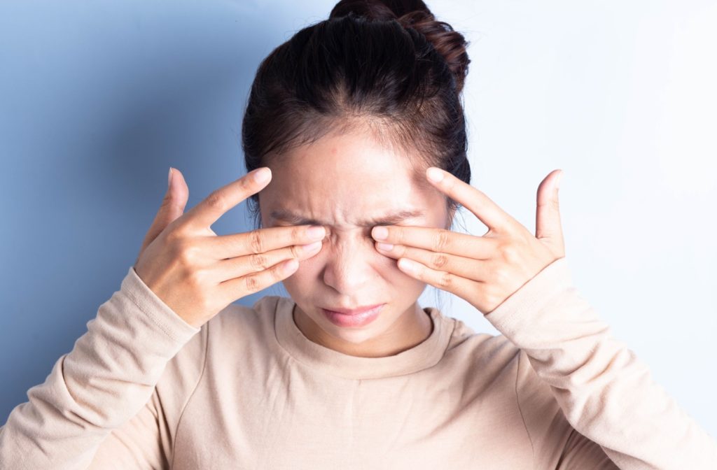 A young woman with dry eye rubs ineffectively at her eyes, trying to get the gritty feeling out