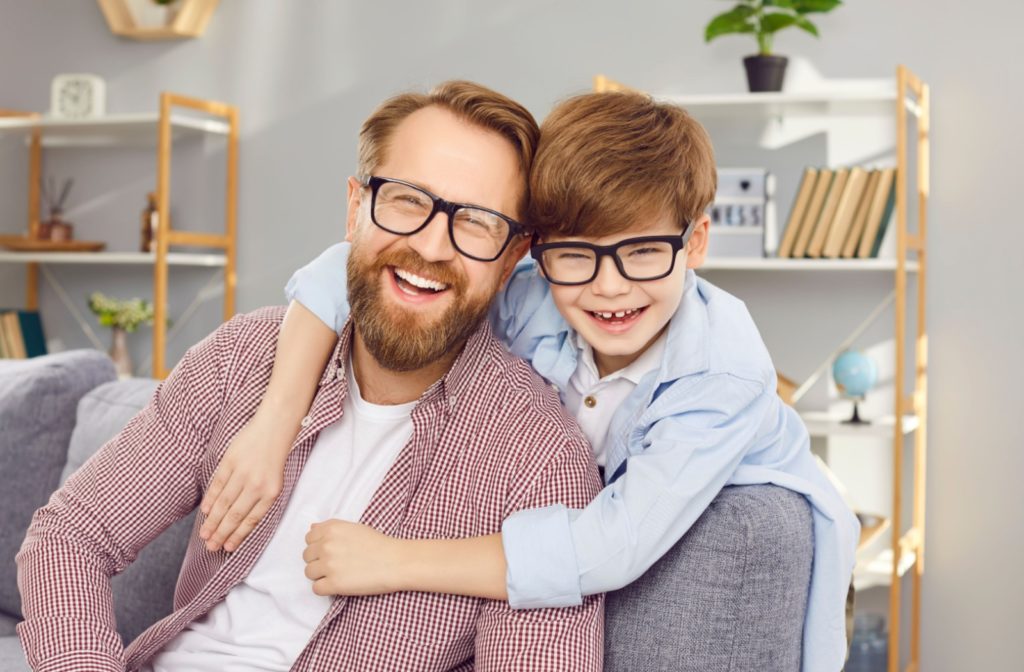 A young child embraces their parent, who is wearing matching eyeglasses.