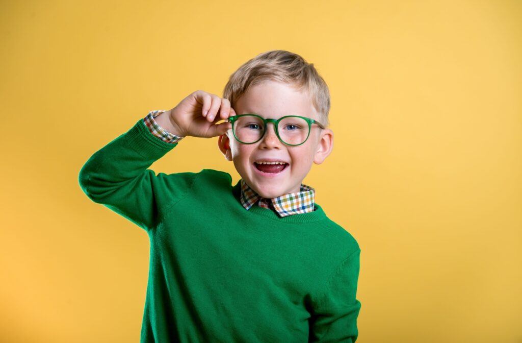 A young, happy child sporting bright green glasses that match their sweater.