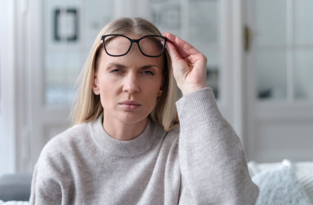A person squints their eyes to try and clearly as they remove their eyeglasses.