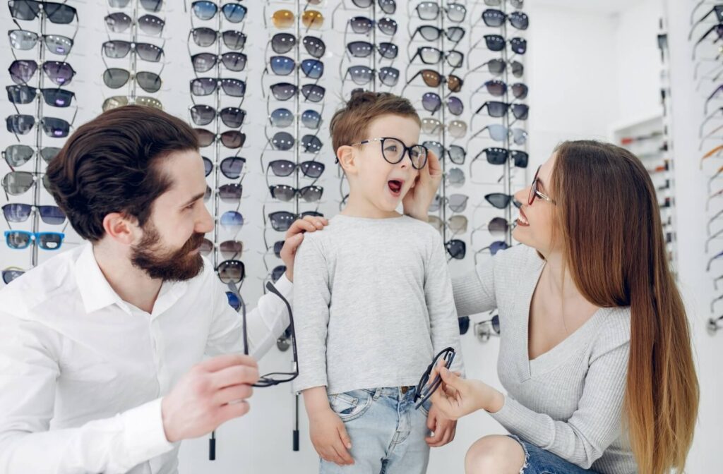 Parents help their child choose between several pairs of glasses.